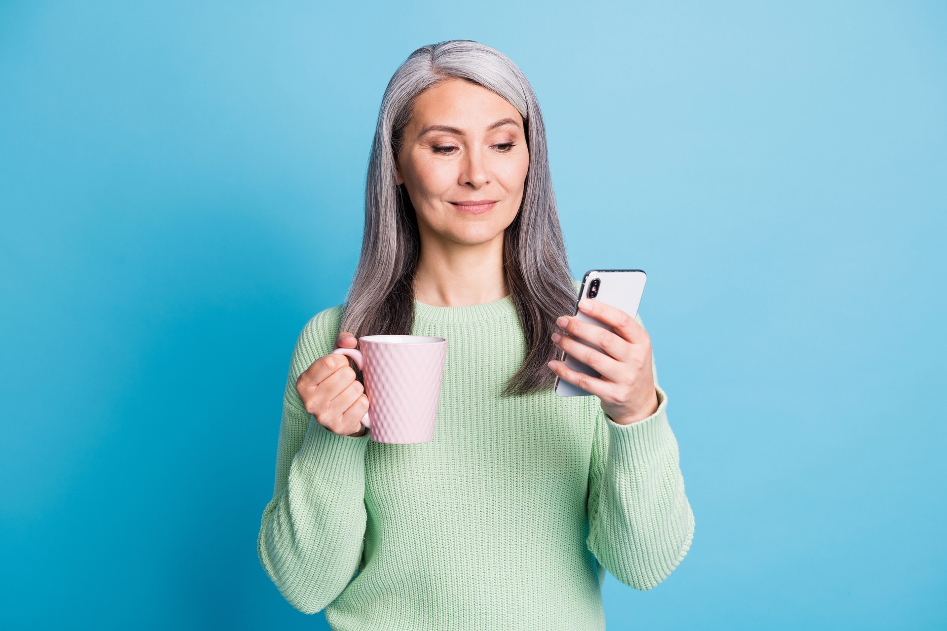 Photo of pensioner old lady hand hold mug telephone look screen wear green pullover isolated blue color background